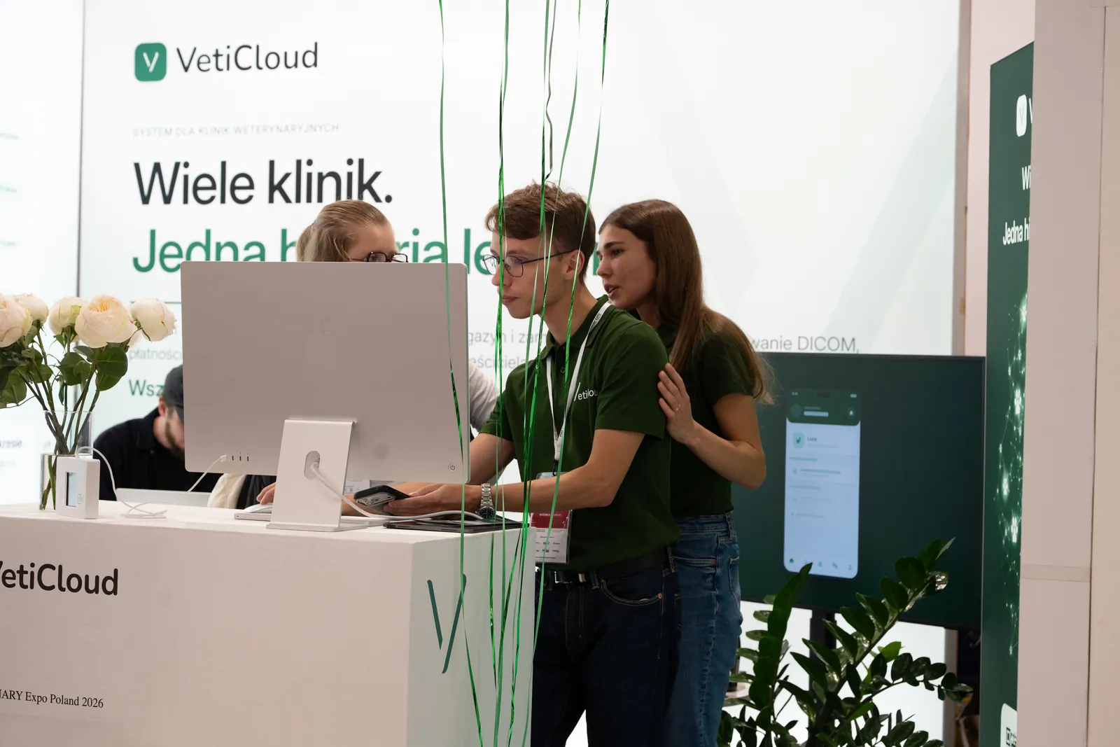 Pokaz programu weterynaryjnego VetiCloud na komputerze przy ladzie stoiska, w tle hasło „Wiele klinik. Jedna historia leczenia.”
